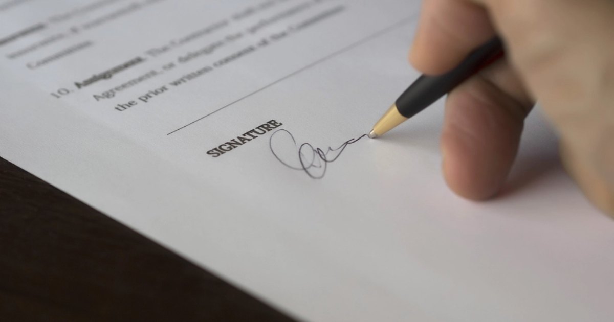 Close up of a person signing the assignment clause of a business agreement